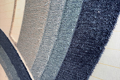 Detailaufnahme eines Teppichs mit Farbverlauf von Beige über Grau bis Marineblau, die Texturen zeigen unterschiedliche Florhöhen
