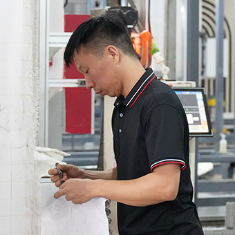 Der Tuftingwerkstatt-Manager in schwarzem Poloshirt mit rot-weißer Borte macht sich Notizen vor einer weißen Wand mit ausrüstung