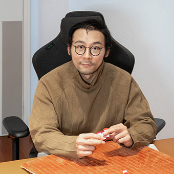 Der Geschäftsführer des Teppichunternehmens sitzt in einem schwarzen Bürostuhl, trägt einen beigen Pullover und eine runde Brille