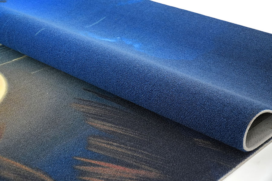 Ein maßgefertigter bedruckter Nylon-Teppich beim Aufrollen, der die blaue Oberseite und einen Teil des darunterliegenden Designs mit blauen, orangefarbenen und dunklen Tönen zeigt und die Textur seiner geschnittenen Flore präsentiert.