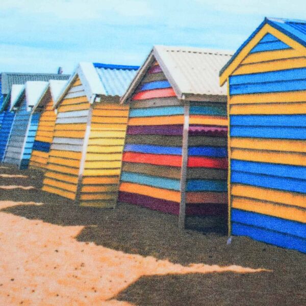 Ein bedruckter Polyesterteppich mit Strandhütten, der sich auf die bunt gestreiften Fassaden mehrerer Hütten (gelb, blau, mehrfarbig) mit ihren charakteristischen Spitzdächern konzentriert.